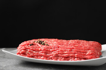 Raw ground meat and peppercorns on grey table, closeup