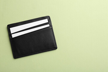 Leather business card holder with blank cards on light green background, top view. Space for text