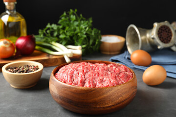 Raw ground meat in bowl and different products on grey table