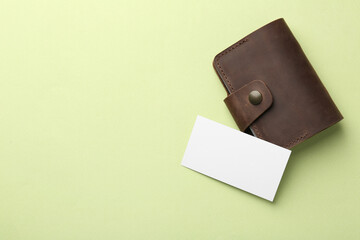 Leather business card holder with blank card on light green background, top view. Space for text