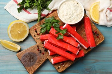 Tasty crab sticks, sauce, pieces of lemon and spices on light blue wooden table, flat lay