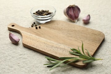 Cutting board, garlic, pepper and rosemary on white textured table. Space for text