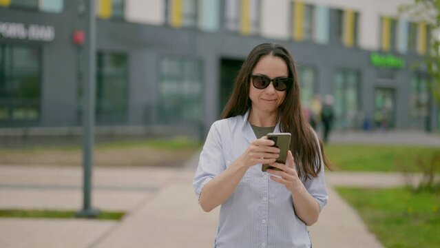 A middle-aged woman wanders around a sleeping area of the city with a phone, without looking up from the screen and spending all her time on the Internet.