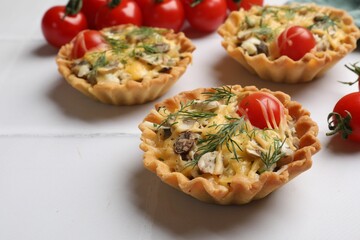 Tasty tartlets with cheese, tomatoes, mushrooms and dill on white tiled table, closeup