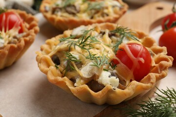 Tasty tartlets with cheese, tomatoes, mushrooms and dill on table, closeup