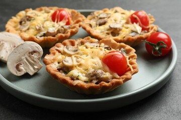 Tasty tartlets with cheese, mushrooms and tomatoes on dark table, closeup