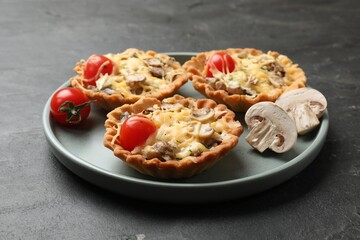 Tasty tartlets with cheese, mushrooms and tomatoes on dark table, closeup