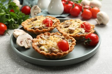Tasty tartlets with cheese, mushrooms and tomatoes on grey table, closeup