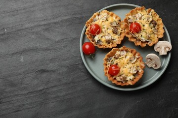 Tasty tartlets with cheese, mushrooms and tomatoes on dark textured table, top view. Space for text