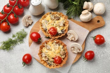 Tasty tartlets with cheese, mushrooms, tomatoes and dill among ingredients on grey table, flat lay