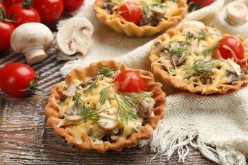 Tasty tartlets with cheese, tomatoes, mushrooms and dill on wooden rustic table, closeup
