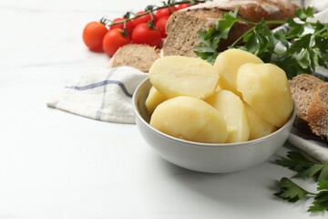 Young boiled potatoes in bowl, bread, tomatoes and parsley on white table, closeup. Space for text