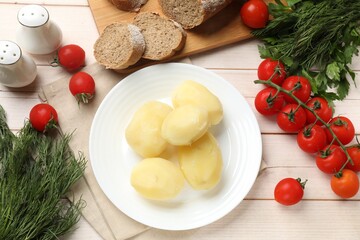 Plate with young boiled potatoes and products on light wooden table, flat lay