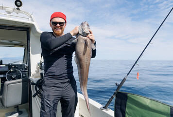 Deep sea sport fishing on yacht in ocean. Happy Male fisherman holding grenadier big fish, Kamchatka Peninsula Russia