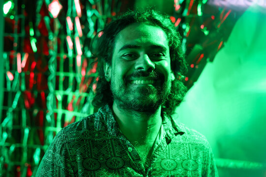 Stylish curly hair man bitting his lip at green neon party