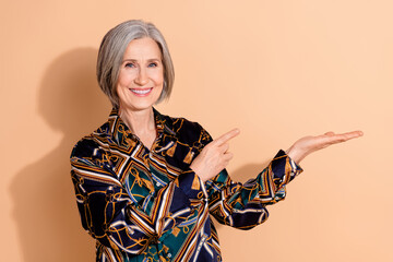 Portrait of senior woman with bob hairdo dressed print shirt indicating at promo on arm empty space...
