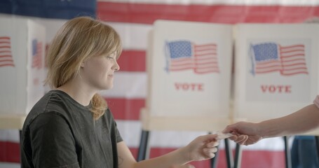 Medium shot, profile, young, red-haired woman, poll worker at voting center, checks identification...