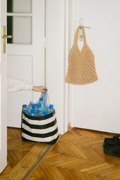 A woman's hand stuffs a crumpled plastic bottle into a paper bag