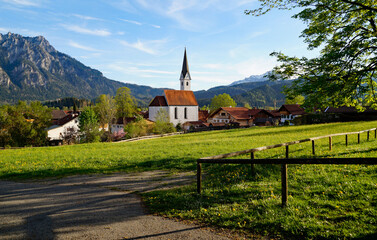 a scenic alpine view with lush green alpine meadows and an old church in the alpine village Schwangau in the Bavarian Alps on a spring evening (Allgaeu, Bavaria, Germany)	