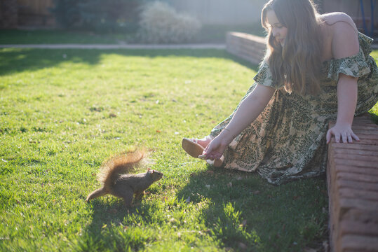 Girl with Long Blonde Hair In A Green Dress Feeds a Squirrel A Penut