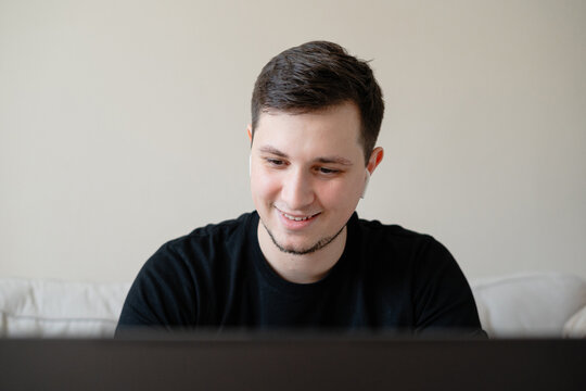 A young smiling man using laptop and wireless headphones