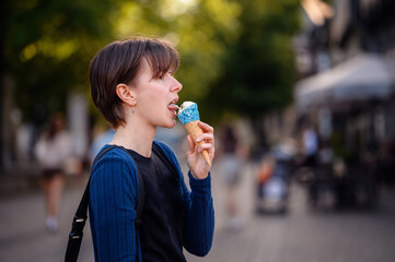 A woman with short hair enjoys an ice cream cone decorated with blue sprinkles on a sunny day in...