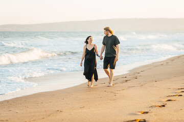 Happy couple walking barefoot along the beach at sunset, holding hands