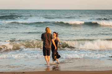 Happy loving couple running along the ocean coastline at sunset