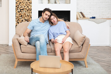 Young married couple sitting on couch and watching movie on laptop. Leisure time and resting...