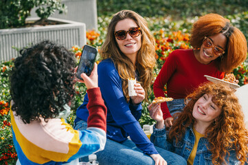 Multicultural friends having a picnic in the park taking photos