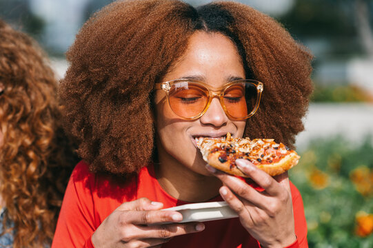 Young Woman Savoring Pizza Outdoors in Sunshine