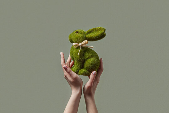 Female hands holding green grass rabbit toy with beige bow in studio