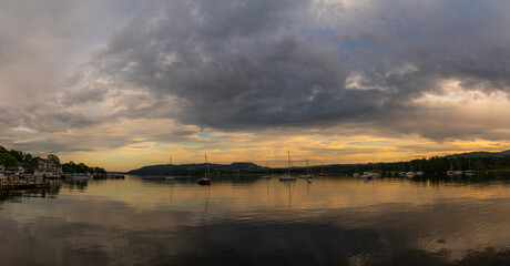 Scenic lake at sunset with boats, cloudy sky, and hills in the background