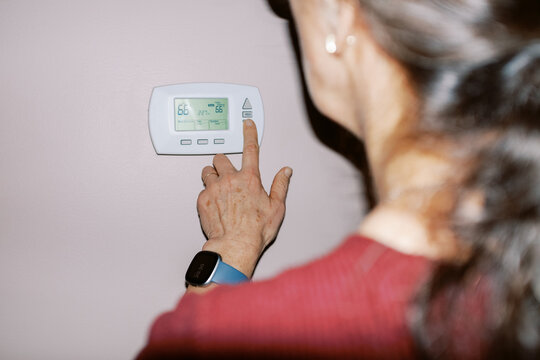 woman in her home changing the temperature on her thermostat