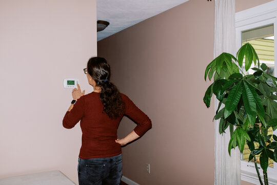 woman in her home changing the temperature on her thermostat