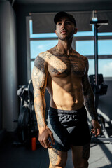 Young, tattooed male with a fit physique poses in a gym