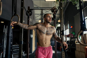 Young, tattooed male with a fit physique poses in a gym