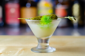 Shaken vodka and pickle juice with ice in a shot glass and garnished with small pickled cucumber and dill