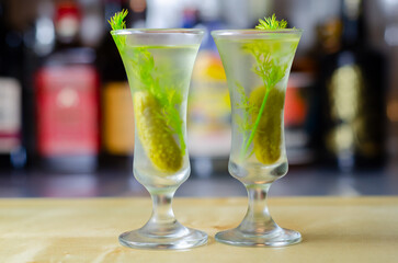 Shaken vodka and pickle juice with ice in a shot glass and garnished with small pickled cucumber and dill