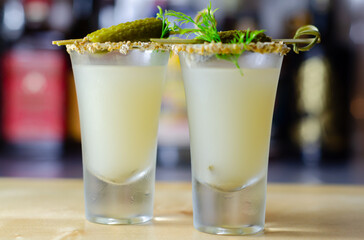 Shaken vodka and pickle juice with ice in a shot glass and garnished with small pickled cucumber and dill