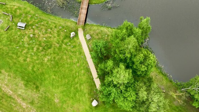 A top-down aerial view of a bridge crossing a small waterway surrounded by grassy areas and trees.