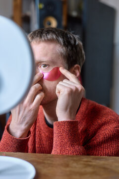 Man applying eye patches  in front of a mirror