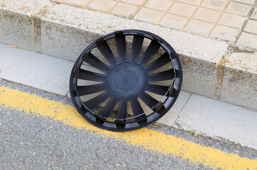 A lost hubcap from a car wheel lies on the side of the road. 