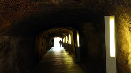 Obraz premium Long underground tunnel with a rock, at the end of the tunnel light and a silhouette of a man are visible
