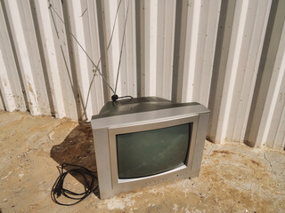 a television sitting outside next to a white building with a gray tv