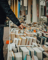 a man looking at many books outside a book market while another person walks by