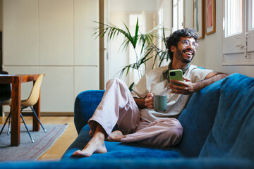 Man with cup of coffee using smartphone at modern flat