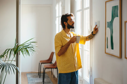 Man adjusting the temperature on the thermostat at home
