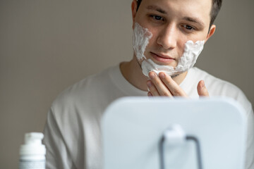 Man applying cleaning or shaving foam on his face in front of mirror