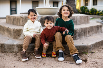 Three young dark haired brothers sit on the steps of a fountain in front of a California adobe in the fall
